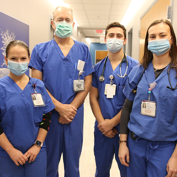 Team of 4 Allied Health professionals stand in hospital hallway.