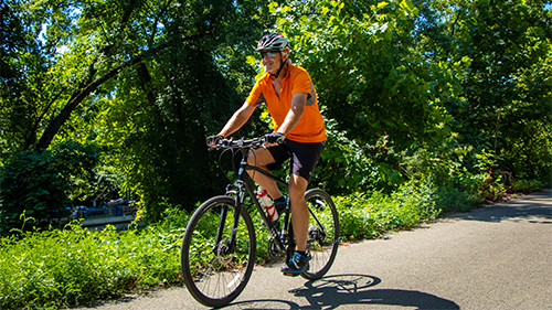 Man bikes outside on a lush bike path.