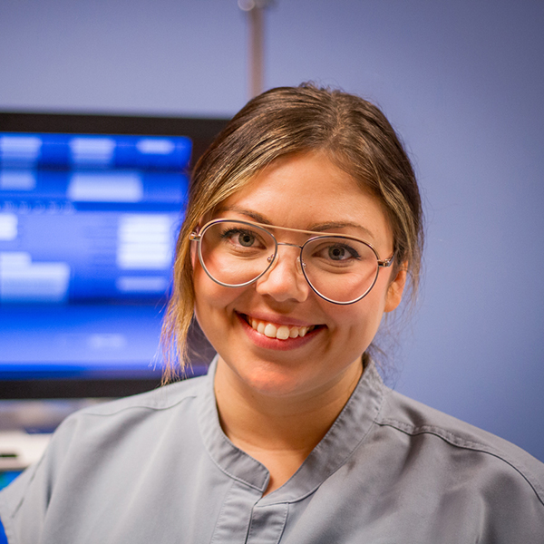 Young woman smiles with imaging equipment in the background.