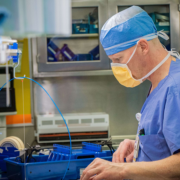 Man in scrubs cleans surgical equipment.