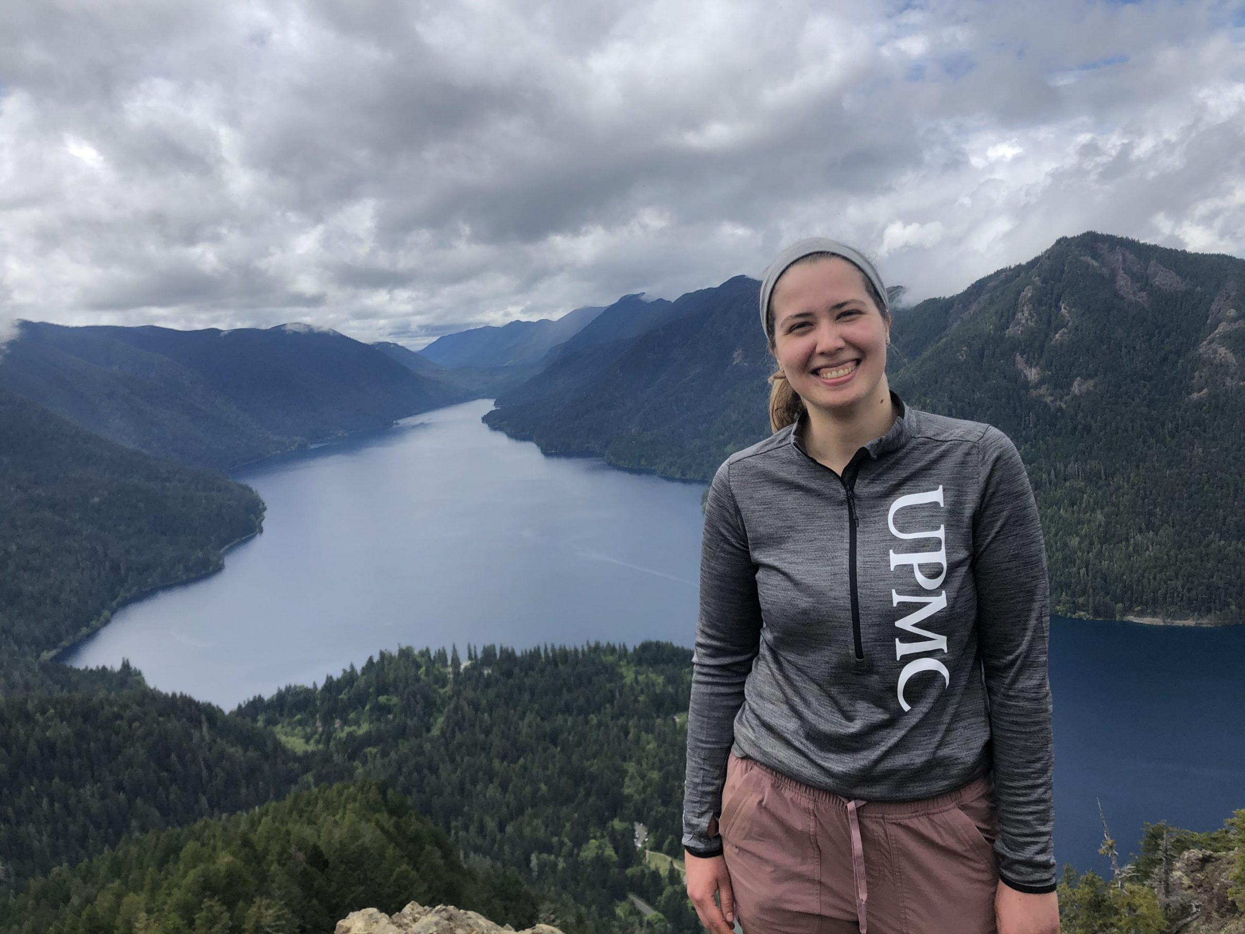 Twenty-something finance employee smiles in front a mountain lake on vacation.