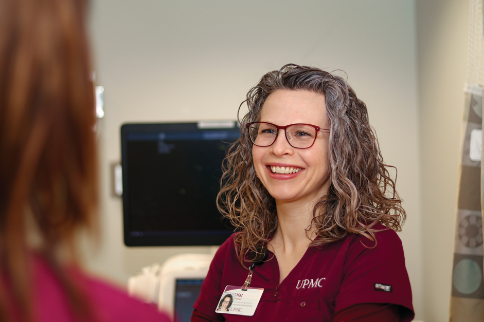 Woman in glasses and red scrubs talks to a colleague.