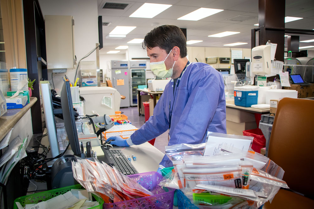 Man stands at desk with a variety of paperwork and samples for testing.