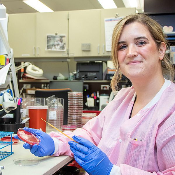Woman in lab smiles while holding sample.
