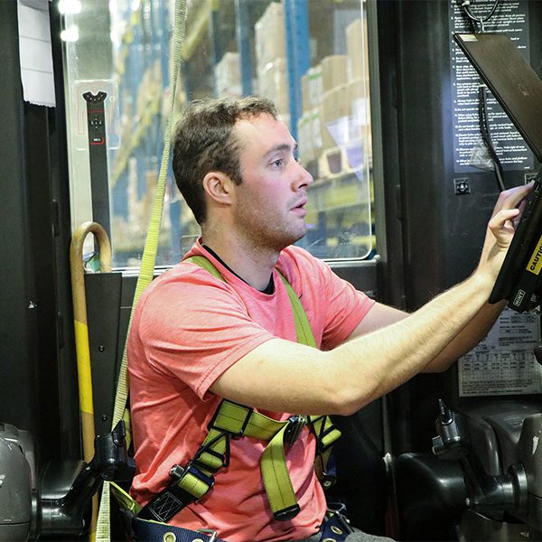 Man sits on forklift equipment in warehouse.