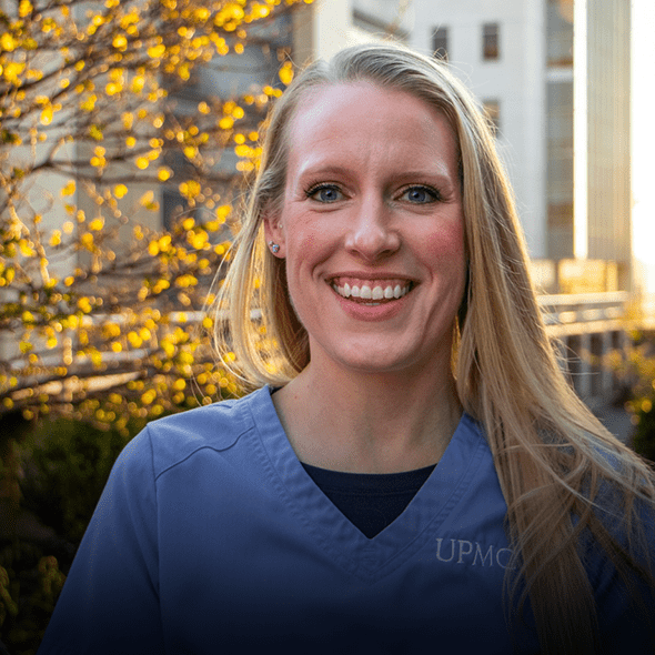 Younger blonde nurse stands outside of hospital while smiling.