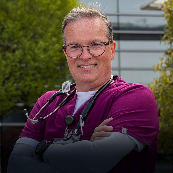 Older nurse with stethoscope stands outside.