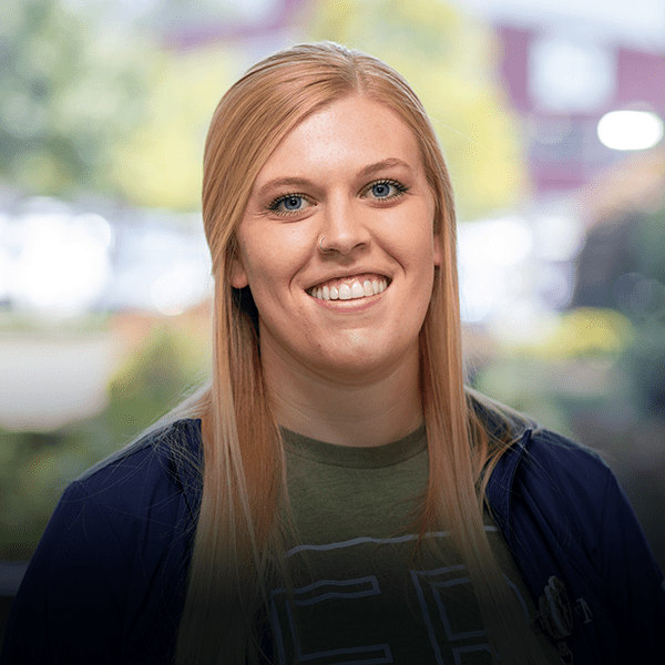 Younger blonde nurse stands outside of hospital.