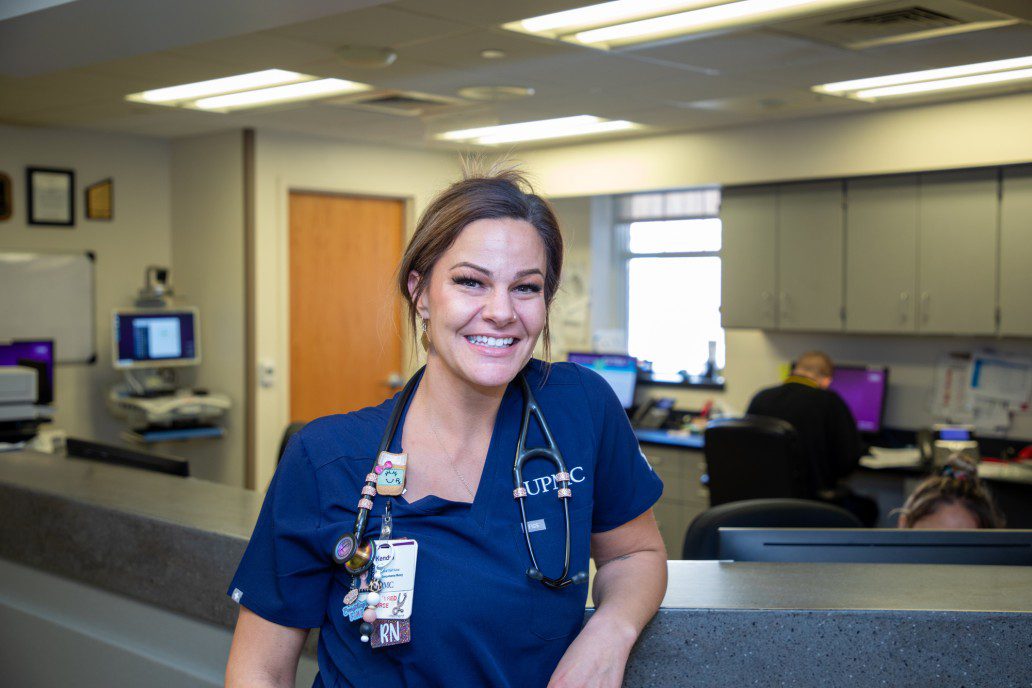 Woman in blue scrubs stands inside at hospital counter.