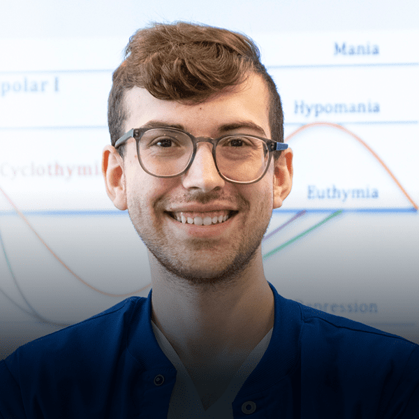 Young man in glasses stands in front of a whiteboard.